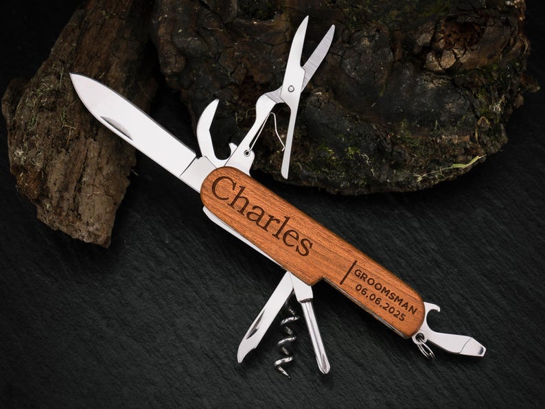 May include: A multi-tool pocket knife with a wooden handle engraved with the name "Charles" and the text "Groomsman 06.06.2025". The knife has a variety of tools, including a blade, a bottle opener, a corkscrew, and a pair of scissors.