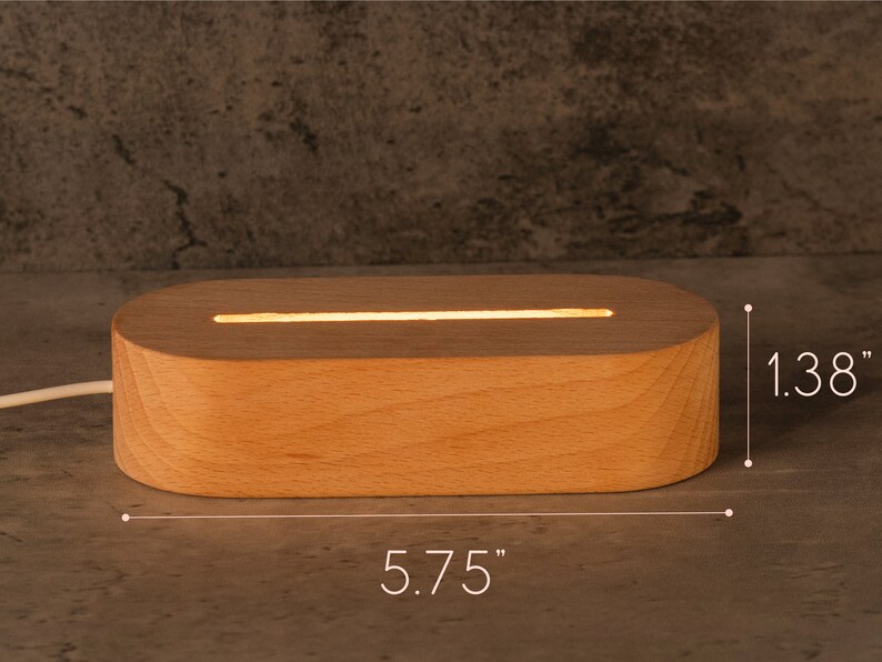 May include: A rectangular wooden LED light base, 5.75 inches long and 1.38 inches high, with a glowing horizontal light strip. The light is made of light-colored wood and has rounded edges. A white power cord extends from the base.