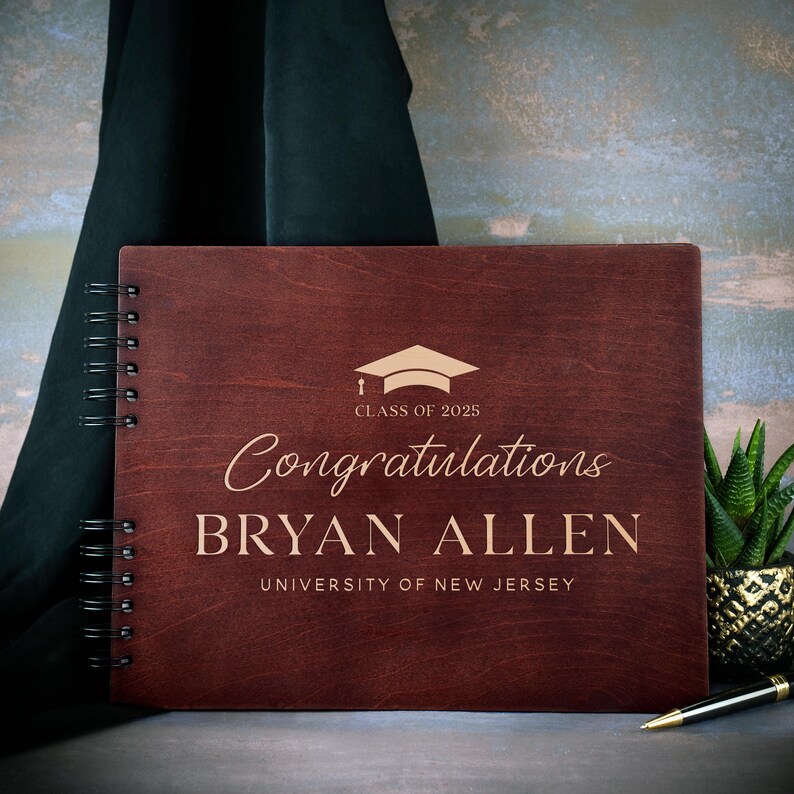 May include: A dark red wooden guest book with a gold graduation cap and the text "Class of 2025" and "Congratulations BRYAN ALLEN UNIVERSITY OF NEW JERSEY".