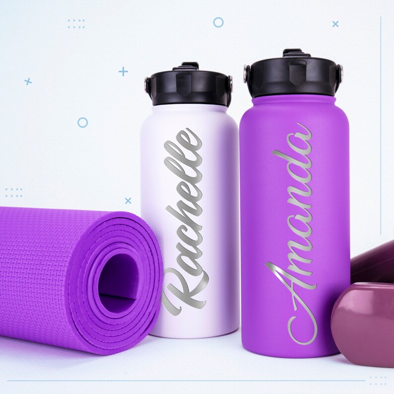 K&ouml;nnte beinhalten: Zwei Wasserflaschen, eine wei&szlig;e und eine violette, mit den personalisierten Namen "Rochelle" und "Amanda", neben einer aufgerollten violetten Yogamatte.