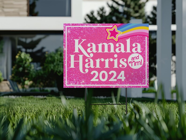 May include: Pink and white yard sign with glitter background. The sign says "Kamala Harris and Tim! 2024" with a rainbow and star graphic.