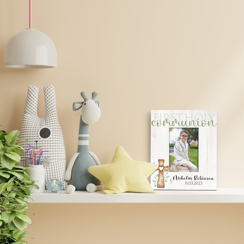 May include: White wooden picture frame with a photo of a boy in a white suit. The frame has the text "First Holy Communion" and a cross with green leaves. The text "Nicholas Robinson 11.03.2023" is below the photo.