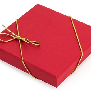 May include: A square red gift box with a matte finish, wrapped with a thin, metallic gold cord tied into a decorative bow on the top surface. The box features sharp, clean edges and a flat lid, presenting a simple and uniform appearance.