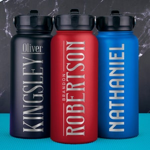 K&ouml;nnte beinhalten: Drei Edelstahl-Wasserflaschen mit personalisierten Namen. Die Flaschen sind schwarz, rot und blau. Die Namen sind Oliver Kingsley, Brandon Robertson und Nathaniel.