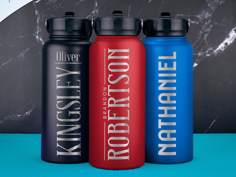 K&ouml;nnte beinhalten: Drei Edelstahl-Wasserflaschen mit personalisierten Namen. Die Flaschen sind schwarz, rot und blau. Die Namen sind Oliver Kingsley, Brandon Robertson und Nathaniel.