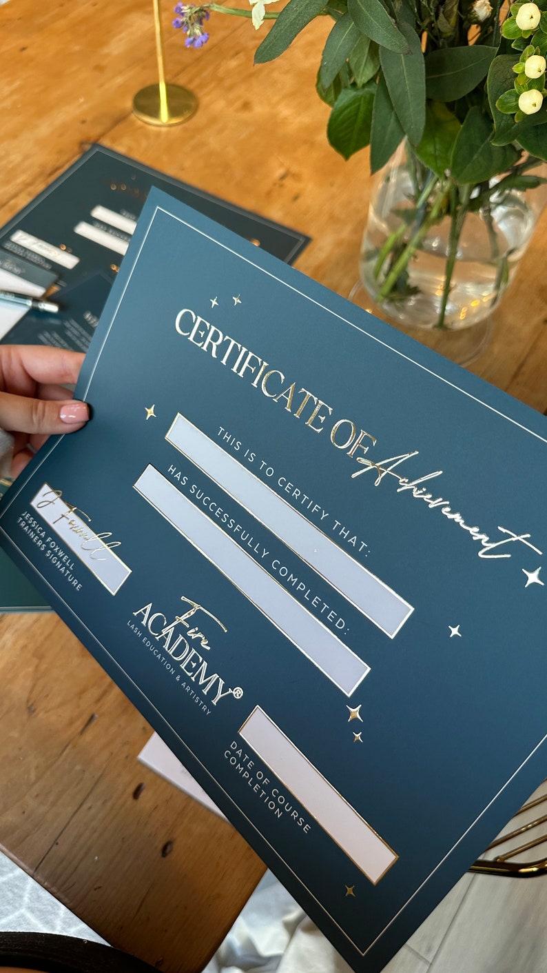 May include: A Certificate of Achievement from Fire Academy, in a dark teal color with gold lettering. The certificate includes spaces for the recipient's name, and the date of course completion. The certificate is held in front of a wooden table.