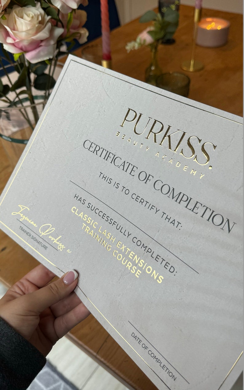 May include: A certificate of completion from Purkiss Beauty Academy for a Classic Lash Extensions Training Course. The certificate has gold lettering and a gold border. The certificate is held by a person.