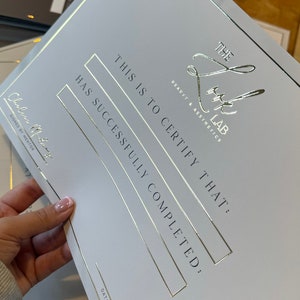May include: A white certificate with gold foil accents. The text reads "THE LUX LAB BEAUTY & AESTHETICS" and "THIS IS TO CERTIFY THAT: HAS SUCCESSFULLY COMPLETED:" The certificate is signed by a mentor.