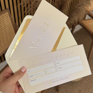 Peut inclure: Un ensemble de certificat cadeau et enveloppe de couleur crème. Le certificat porte l'inscription "Meraki" en dorure à chaud, avec "Grace Berry Skin & Lash House" en dessous. L'enveloppe a une doublure dorée. Le certificat a de l'espace pour le destinataire, l'expiration et un message.