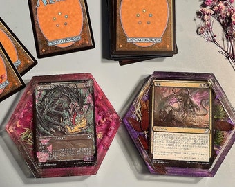 May include: Two hexagonal resin coasters with a purple and pink border. Each coaster features a different Magic: The Gathering card. The card on the left is a green and black creature card with the text "グール・サーヴァント". The card on the right is a black and white creature card with the text "イシュトヴァーン".