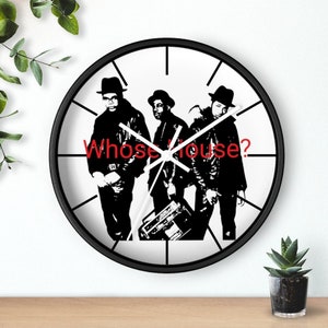 May include: Black and white clock featuring a silhouette of three people with the text "Whose house?" in red. The clock has black hands and a black frame.