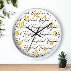 May include: White round clock with black hands and black script that says "Beyhive" repeatedly. The numbers 1 through 12 are in yellow and are surrounded by small yellow bees.