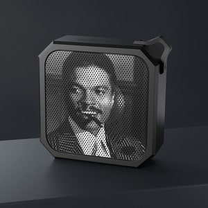 May include: A black portable speaker with a metal grille and a black and white photo of a man on the front.