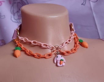 May include: A pink and orange plastic chain necklace with a pink bunny charm holding a carrot. The necklace has two carrot charms hanging from it.