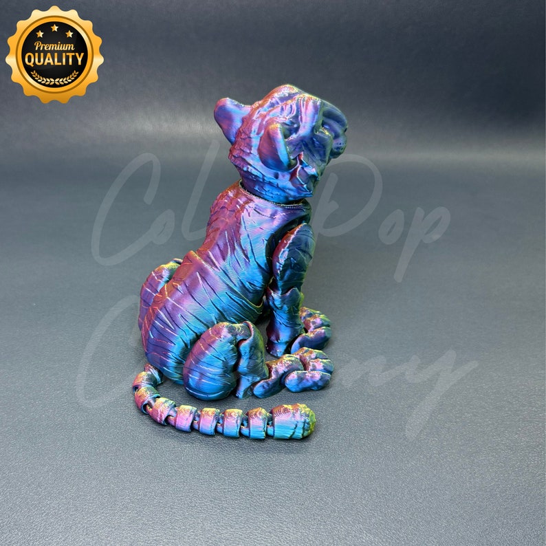 May include: A small, iridescent purple, blue, and green 3D printed tiger figurine sitting on a gray surface. The tiger is looking up and has a curled tail.