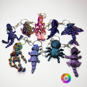 May include: A collection of nine articulated keychains featuring various creatures including a skeleton, a robot, a spider, and a dragon. Each keychain is crafted from iridescent, multi-coloured plastic with a metallic finish and a silver metal clasp.