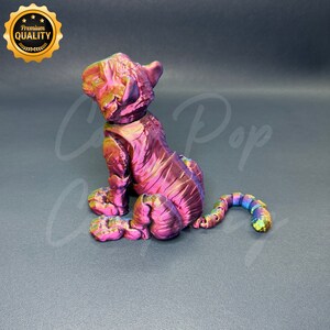 May include: A small, iridescent pink and purple tiger figurine with a curled tail. The figurine is made of a shiny, metallic material and has a detailed, textured surface.