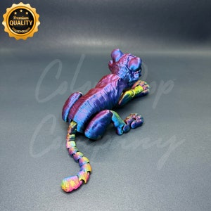 May include: A 3D printed iridescent tiger figurine with a segmented tail. The figurine is posed in a crouching position with its head turned to the side.