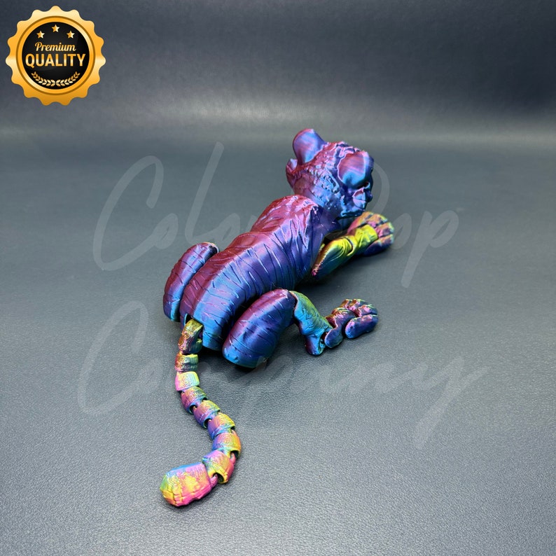 May include: A 3D printed iridescent tiger figurine with a segmented tail. The figurine is posed in a crouching position with its head turned to the side.