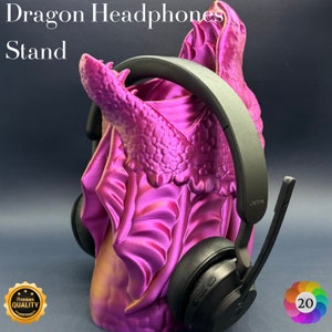May include: A purple dragon-shaped headphone stand with a black Jabra headset resting on it. The stand is made of 3D printed plastic and has a textured, scaly surface. The headset has a black headband and earcups, and a silver microphone boom.