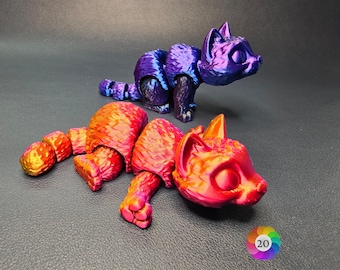 May include: Two 3D printed figurines of cats, one in a vibrant red and orange gradient and the other in a deep purple and blue gradient. The figurines are posed in a playful manner, with the red and orange cat lying down and the purple and blue cat standing on its hind legs.