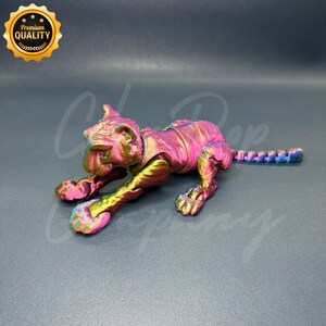 May include: A metallic pink and green tiger figurine with a textured surface. The figurine is posed in a crouching position with its head turned to the side.