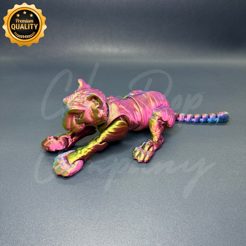 May include: A metallic pink and green tiger figurine with a textured surface. The figurine is posed in a crouching position with its head turned to the side.