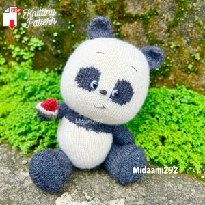 May include: A white and gray knitted panda bear plush toy holding a red watermelon slice. The panda has black eyes and a black nose. The toy is sitting on a green mossy surface.