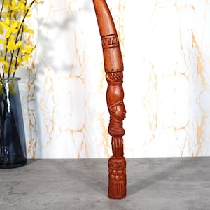 Puede incluir: Una escultura de madera alta y tallada intrincadamente con un rico acabado marrón. La escultura presenta una parte superior cónica, patrones geométricos y un rostro humano detallado. Se alza verticalmente, mostrando la artesanía.