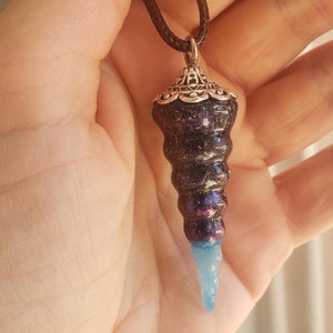 May include: A black and iridescent seashell pendant necklace with a silver-toned metal top and a blue tip. The necklace is on a brown cord.