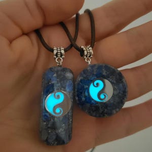 Könnte beinhalten: Zwei Halsketten mit im Dunkeln leuchtenden Yin-Yang-Anhängern. Die Anhänger sind aus blauem Lapislazuli-Stein mit silbernen Akzenten.