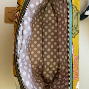 May include: A mustard yellow fabric pouch with a green zipper and a white polka dot lining. The pouch has a floral print with pink, green, and white accents.