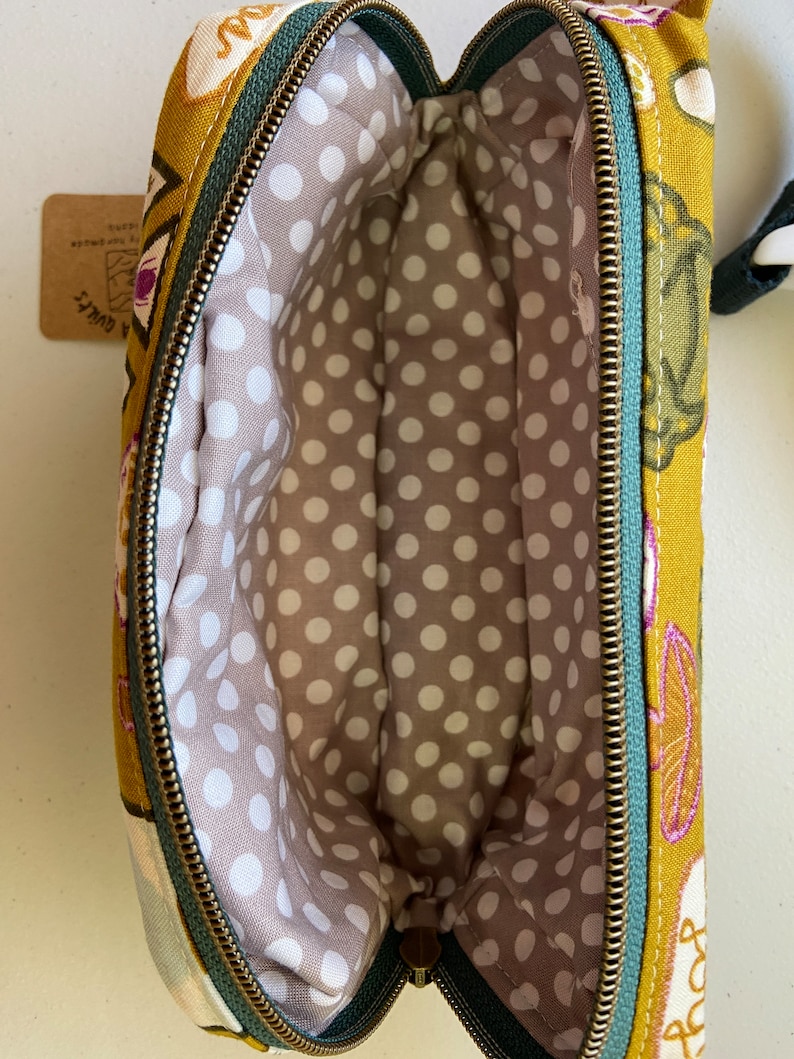 May include: A mustard yellow fabric pouch with a green zipper and a white polka dot lining. The pouch has a floral print with pink, green, and white accents.