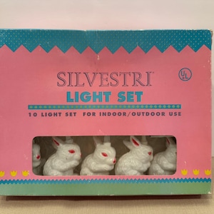 May include: A vintage light set by Silvestri, featuring ten white bunny lights with red eyes. The box is pink with a teal top and bottom, and the text "SILVESTRI LIGHT SET" is displayed on the front. For indoor/outdoor use.