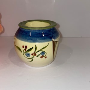 May include: A white ceramic oil burner with a blue and green rim. The burner has a floral design with red and blue accents.