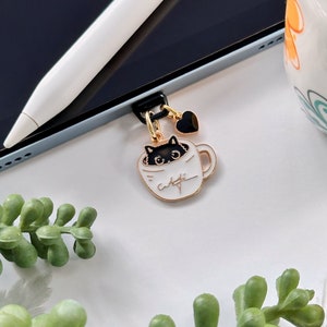 May include: A gold-tone charm with a black cat peeking out of a white coffee cup with the word "caffe" written on it. The charm is attached to a black stylus holder.