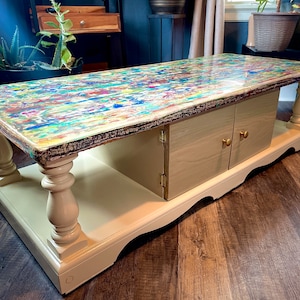 May include: A colorful coffee table with a unique abstract design on the top. The table has a lower shelf and two doors with gold knobs.