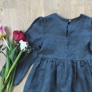 May include: A blue linen dress with long sleeves and a gathered skirt. The dress has a button closure in the back.