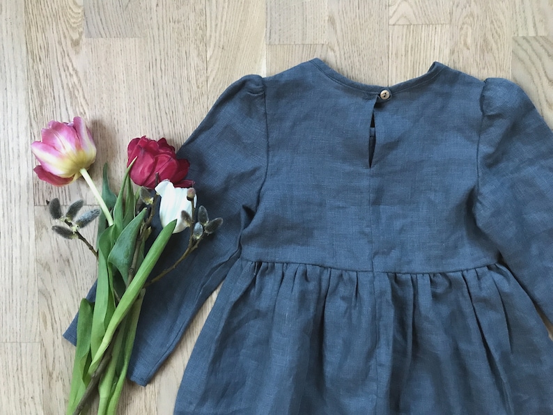 May include: A blue linen dress with long sleeves and a gathered skirt. The dress has a button closure in the back.