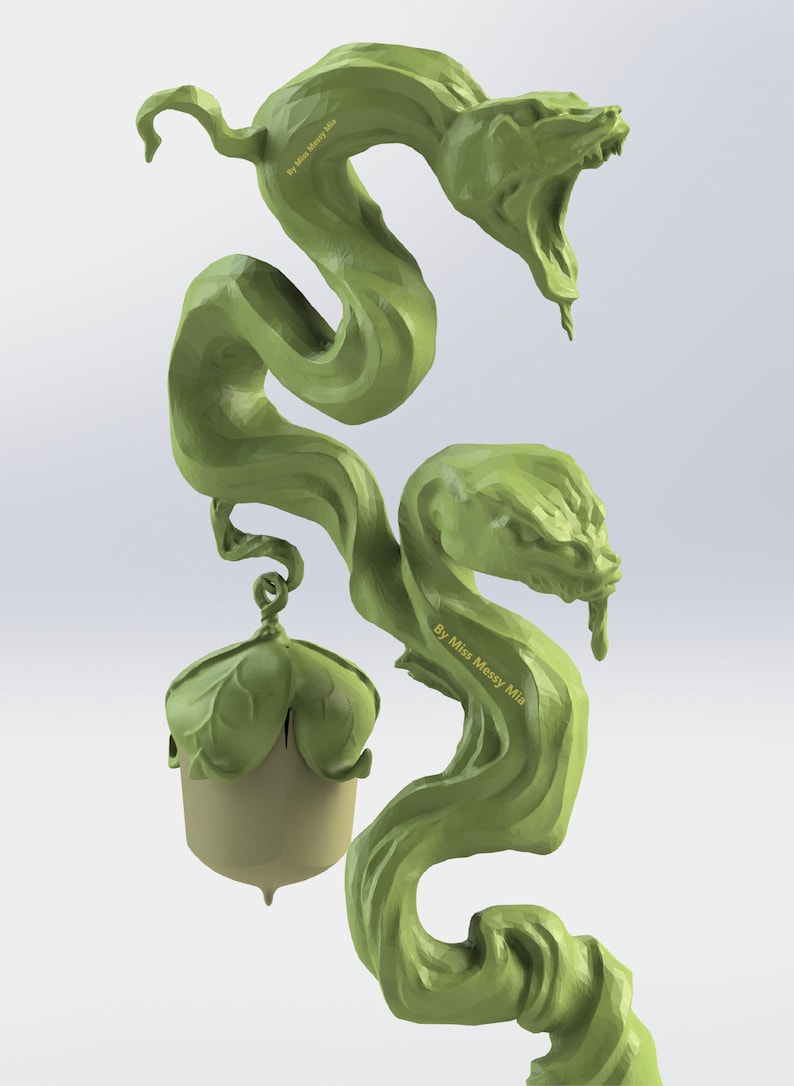 Puede incluir: Una escultura verde impresa en 3D de una vid con dos cabezas de serpiente y una bellota en la parte inferior. La vid est&aacute; enroscada y retorcida, y las cabezas de serpiente tienen la boca abierta y dientes afilados. La bellota es marr&oacute;n y tiene una tapa verde. La escultura est&aacute; firmada "By Miss Messy Mia".