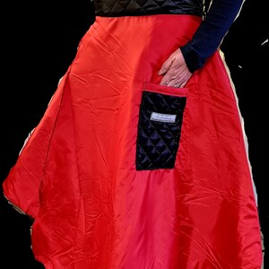 Pode incluir: Uma saia vermelha acolchoada com um bolso acolchoado preto. O bolso tem uma etiqueta branca com o texto "Handmade in Netherlands".
