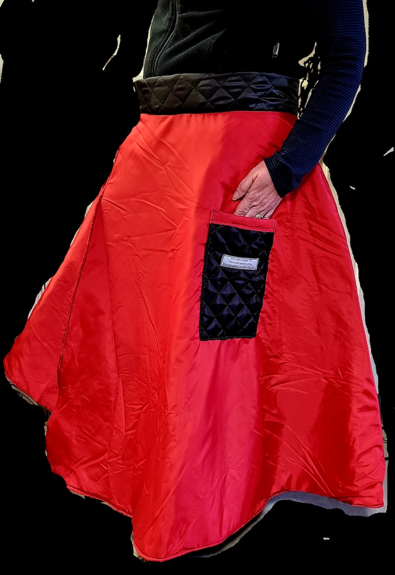 Pode incluir: Uma saia vermelha acolchoada com um bolso acolchoado preto. O bolso tem uma etiqueta branca com o texto "Handmade in Netherlands".
