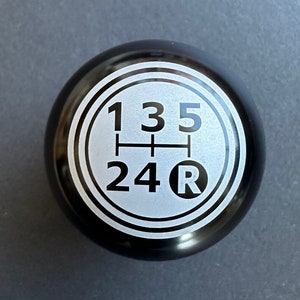May include: Black gear shift knob with a silver gear pattern and the numbers 1, 3, 5, 2, 4, and the letter R.