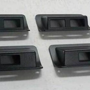 May include: Four black plastic switch plates with rectangular cutouts for toggle switches. The plates have a slightly curved shape and are designed to be mounted on a wall or surface.