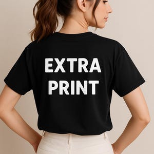 Puede incluir: Camiseta negra con el texto blanco "EXTRA PRINT" en la espalda. La modelo lleva pantalones de color claro. La camiseta tiene mangas cortas y cuello redondo.