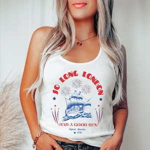 May include: White tank top with a patriotic design featuring a ship, fireworks, and text that reads "Jo Long London Had a Good Run Signed, America 1776". The design is in red, white, and blue.