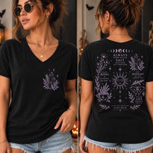 May include: A black V-neck t-shirt featuring a small purple crystal graphic on the front left chest. The back displays a large purple celestial design with a sun, moon phases, crystals, flowers, a moth, and text including Always Throw Spilled Salt.