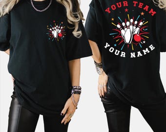 May include: Black t-shirt featuring a bowling design. The front has a small graphic of bowling pins and a ball with colorful starbursts. The back displays "YOUR TEAM" and "YOUR NAME" above and below a larger bowling graphic. A fun shirt for bowling enthusiasts.
