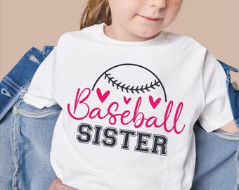 May include: White t-shirt with a baseball design. The design includes a black baseball, pink hearts, and the words "Baseball Sister" in pink and black. The shirt is worn by a young person.