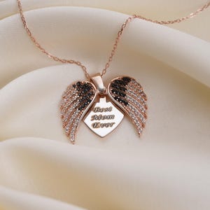 A necklace with a pendant featuring a heart-shaped design with wings and the words "Best Mom Ever" engraved on it, placed on a white fabric background.